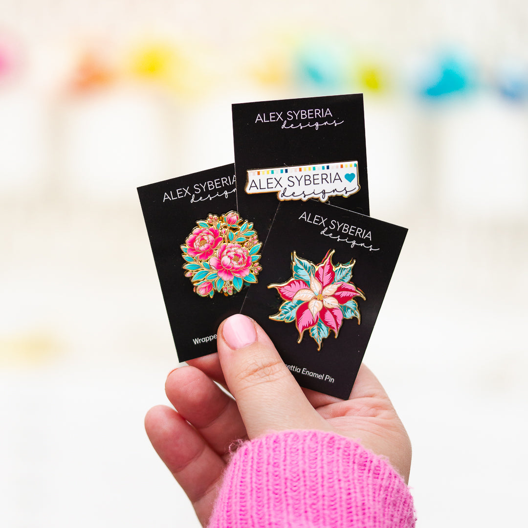 floral enamel pins with 'Alex Syberia Designs' packaging. Festive Poinsettia Wrapped with Love enamel pins
