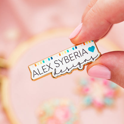 Enamel Pin with 'ALEX SYBERIA designs logo beautiful