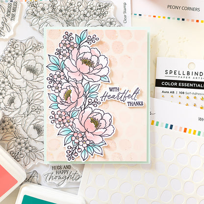 A handmade floral greeting card with layered pink Peony Corners Stamp set by Alex Syberia, and a stencil dots, and the text 'with Heartfelt Thanks' and 'Hugs and Happy thoughts,' styled on top of crafting supplies including clear stamp sheets, adhesive, and branded Alex Syberia Designs and Spellbinders.