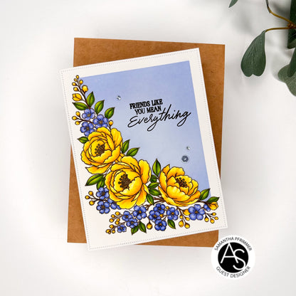 A handmade greeting card with a floral design featuring yellow peonies, blue forget-me-nots, and green leaves on a light blue background with the text 'FRIENDS LIKE YOU MEAN Everything'. The card is displayed on top of a brown kraft envelope on a white surface with a green plant leaf in the corner.Alex Syberia Designs Stamps and dies press plates.